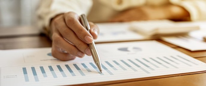 A man's hand holding a pen over a piece of paper with a graph on it